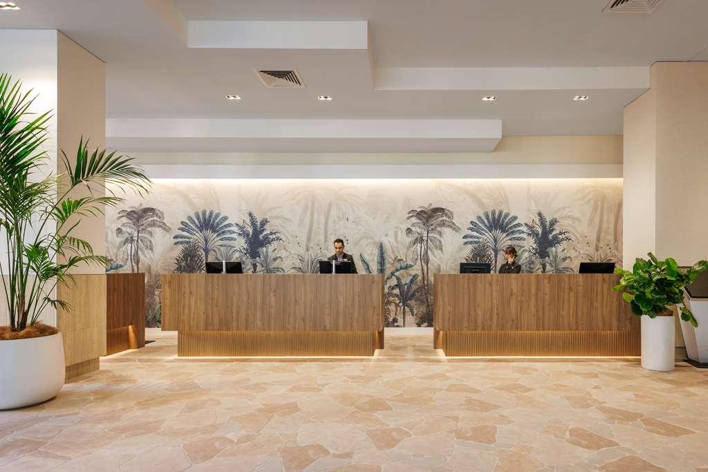 Amora Hotel Brisbane Interior foto The photo shows a modern reception area with two wooden reception desks. Behind the desks, there is a decorative wall featuring a large mural of tropical plants and palm trees, creating a serene atmosphere. The space is well-lit with overhead lights,